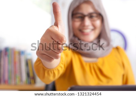 Portrait of Asian muslim businesswoman working on laptop at the office, smiling happy expression with thumb up ok sign gesture