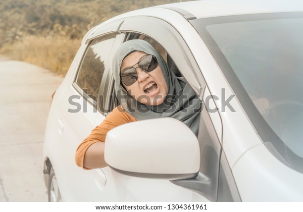 Portrait\
of Asian muslim lady driver getting mad and angry from the traffic,\
screaming and showing rude gesture from her\
car