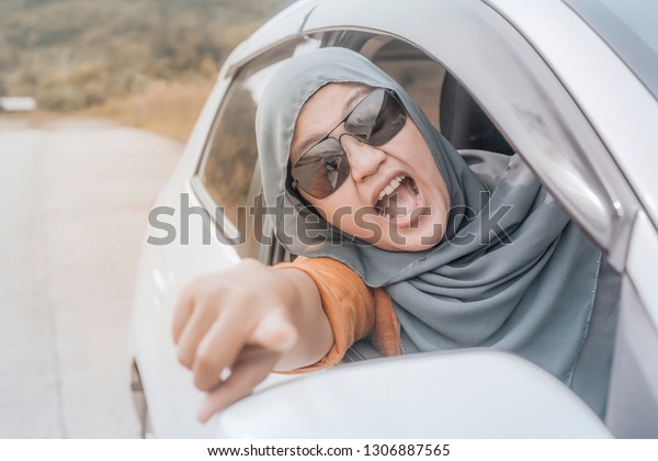 Portrait\
of Asian muslim lady driver getting mad and angry from the traffic,\
screaming and showing rude gesture from her\
car