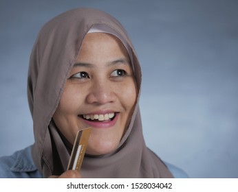 Portrait of Asian muslim woman smiling and thinking while holding credit card