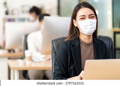 Portrait of asian office employee businesswoman wear protective face mask work in new normal office with interracial colleague in background as social distance practice prevent coronavirus COVID-19.