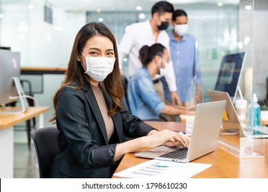 Portrait of asian office employee businesswoman wear protective face mask work in new normal office with interracial team in background as social distance practice prevent coronavirus COVID-19. - Shutterstock ID 1798610230