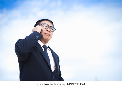 Portrait Of Asian Old Man In Black Suit Talking With Someone On Mobile Phone.Communication Concept.