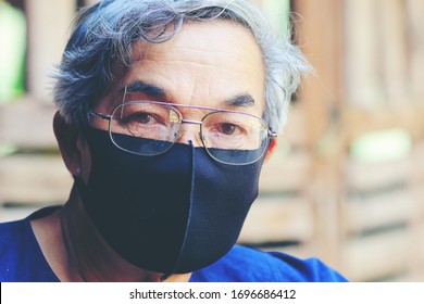 Portrait Of An Asian Old Man, More 60 Years Old, In A Face With A Black Cloth Mask . A Concept Of The Danger Of Coronavirus For The Elderly.Covid-19 Outbreak Contamination Concept.