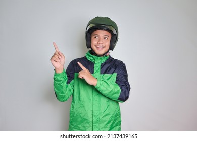 Portrait Of Asian Online Taxi Driver Wearing Green Jacket And Helmet Pointing At Empty Space With Finger. Isolated Image On White Background