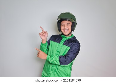 Portrait Of Asian Online Taxi Driver Wearing Green Jacket And Helmet Pointing At Empty Space With Finger. Isolated Image On White Background