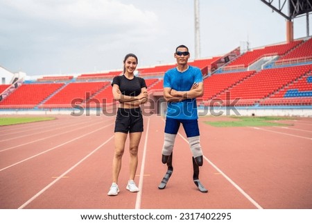 Portrait of Asian para-athlete disabled and trainer standing in stadium. Attractive amputee male runner and young sportswoman smiling, looking at camera after practicing for Paralympics competition.