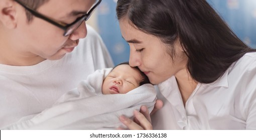 Portrait Asian Parents Mom Kiss Newborn Baby, Closeup Portrait Of Young Couple Father Mother Holding Kissing New Born Baby In Hospital Bed. Happy Asia Family Love Newborn Nursery Mother’s Day Holiday 