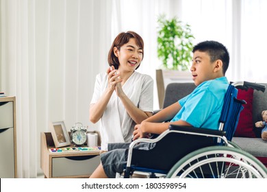 Portrait Of Asian Physiotherapist Carer Helping And Playing With Special Disabled Child Health Problem By Doing Exercises Sitting In Wheelchair In Rehabilitation Clinic.disability Care Concept