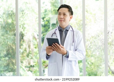 Portrait Of Asian Senior Doctor Standing In Medical Office While Using Tablet.