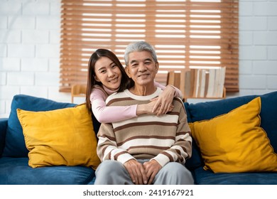 Portrait of Asian senior father sitting on sofa with daughter in house. Attractive beautiful granddaughter feeling happy and relax, enjoy visit older mature grandparent and looking at camera at home. - Powered by Shutterstock