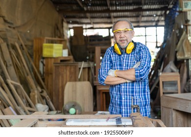 Portrait Of Asian Senior Male Carpenter Worker Wearing Safety Goggles And Earmuffs At Work. Asian Male Woodworker. Asian Male Craftsman