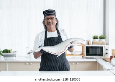 Portrait of Asian senior man chef is holding and showing fresh whole salmon in his hands smiling at camera and standing in kitchen. Elderly chef prepare fish for ingredient in japanese food concept - Powered by Shutterstock