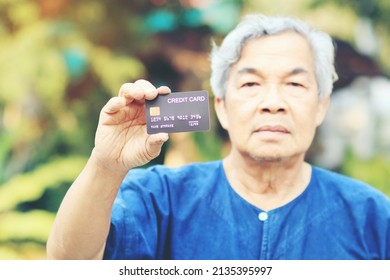 Portrait Of An Asian Senior Man, More 60 Years Old, Holding Black Credit Card And Showing On Hand And Looking At Camera Feeling Enjoy. Elderly Financial Lifestyle Concept. Vintage Tone Colour.