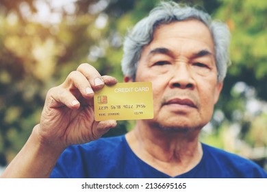 Portrait Of An Asian Senior Man, More 60 Years Old, Holding Golden Credit Card And Showing On Hand And Looking At Camera Feeling Enjoy. Elderly Financial Lifestyle Concept With Copy Space In Left Side