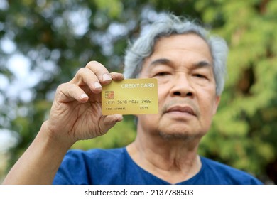 Portrait Of An Asian Senior Man, More 60 Years Old, Holding Golden Credit Card And Showing On Hand And Looking At Camera Feeling Enjoy. Elderly Financial Lifestyle Concept With Copy Space In Left Side