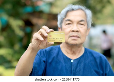 Portrait Of An Asian Senior Man, More 60 Years Old, Holding Golden Credit Card And Showing On Hand And Looking At Camera Feeling Enjoy. Elderly Financial Lifestyle Concept With Copy Space In Left Side