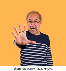 Portrait Of Asian Senior Man Wearing Glasses Standing Face Expression And Hand Rising Posing Show Stop Symbol Isolated On Yellow Background. Elderly Male Palm Up With Forbidden, Refusal And Excited.