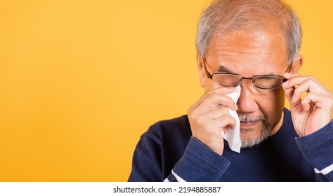 Portrait Asian Senior Old Man Sad Wiping Away His Tears Studio Shot Isolated On Yellow Background, Elder Man Crying Raise Glasses With Tissue Wipe Red Eyes, Sadness Depressed Lonely