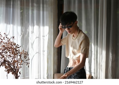 Portrait Of Asian Slim Teenager With Crop Top Cream Shirt And Sunglasses Standing And Posing In The Modern Interior Room, People Lifestyle Fashion LGBTQ Concept.