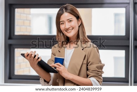Portrait Asian smart beautiful businesswoman wearing casual business clothes, holding cup of coffee, smiling with happiness, confidence, standing in modern indoor office