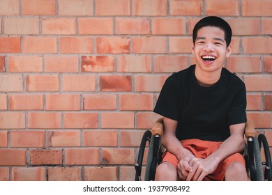 Portrait of Asian special child on wheelchair is smiling face as happiness on orange brick wall at the house, Lifestyle in the education age of disabled children, Happy disability kid concept.