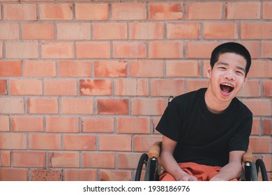 Portrait Of Asian Special Child On Wheelchair Is Smiling Face As Happiness On Orange Brick Wall At The House, Lifestyle In The Education Age Of Disabled Children, Happy Disability Kid Concept.