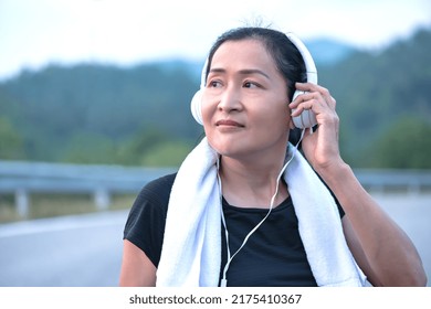 Portrait Asian Sporty Woman With Headphones Running On Dam Ridge, Middle Aged Asian Female Exercising, Fitness Woman Workout, Female Runner, Lady Jogging At Dam, Sports And Recreation Concept 