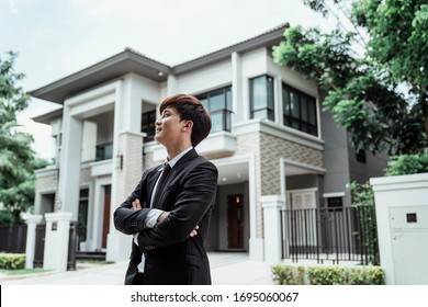 Portrait Of Asian Successful Businessman With A Big House At Background. Rich Guy With Gigantic House.