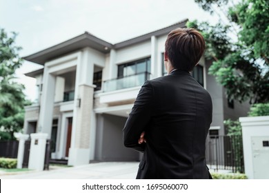 Portrait Of Asian Successful Businessman With A Big House At Background. Rich Guy With Gigantic House.