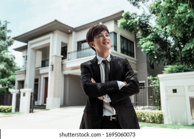 Portrait Of Asian Successful Businessman With A Big House At Background. Rich Guy With Gigantic House.