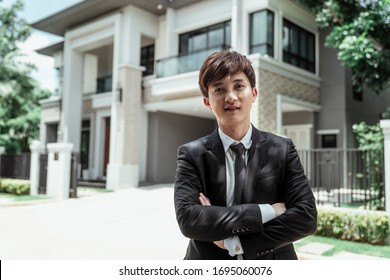 Portrait Of Asian Successful Businessman With A Big House At Background. Rich Guy With Gigantic House.