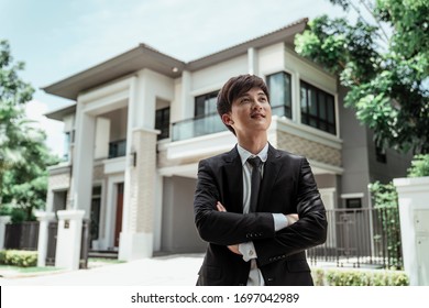 Portrait Of Asian Successful Businessman With A Big House At Background. Rich Guy With Gigantic House.