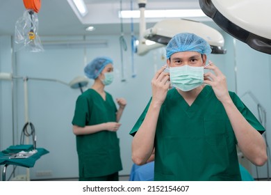 Portrait Of Asian Surgeon With Medical Mask Standing In Operation Theater At A Hospital. Team Of Professional Surgeons. Healthcare, Emergency Medical Service Concept