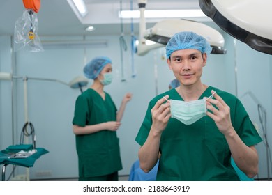 Portrait Of Asian Surgeon With Medical Mask Standing In Operation Theater At A Hospital. Team Of Professional Surgeons. Healthcare, Emergency Medical Service Concept