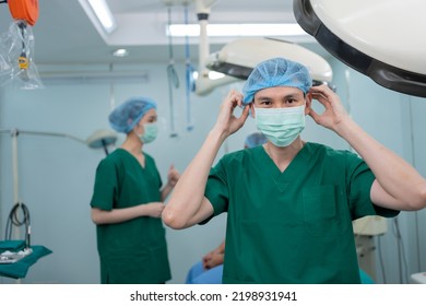 Portrait Of Asian Surgeon With Medical Mask Standing In Operation Theater At A Hospital. Team Of Professional Surgeons. Healthcare, Emergency Medical Service Concept