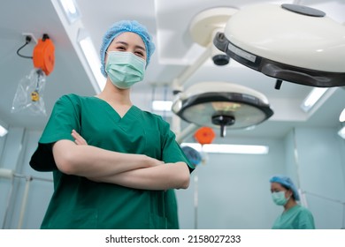 Portrait Of Asian Surgeon And Nurse With Medical Mask Standing With Arms Crossed In Operation Theater At A Hospital. Team Of Professional Surgeons. Healthcare, Emergency Medical Service Concept