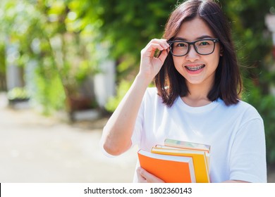 Portrait Of Asian Teen Beautiful Young Woman Wear Eyeglasses Smile Have Dental Braces On Teeth Laughing At Outdoor She Hold Education Books On Hand, Medicine And Dentistry Concept