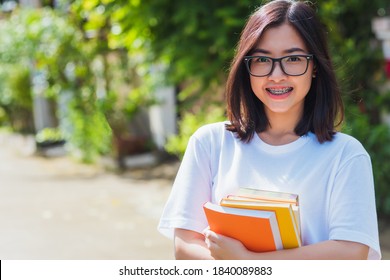 Portrait of Asian teen beautiful young woman wear eyeglasses smile have dental braces on teeth laughing at outdoor she hold education books on hand, Medicine and dentistry concept