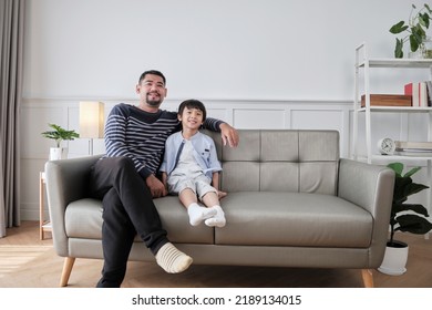 Portrait Of Asian Thai Family, One Adult Dad And Little Son Happiness Home Living Together, Relaxing And Smile, Leisure On Sofa In House's White Room, Lovely Weekend And Wellbeing Domestic Lifestyle.