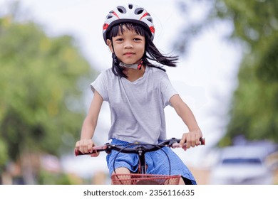 Portrait of Asian Thai kid girl Cute and bright face, 6 to 8 years old, riding a red bicycle outdoors. She enjoys riding exercise bikes to learn balance and strong body The background is a green tree. - Powered by Shutterstock