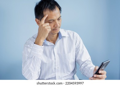 Portrait Of An Asian Thai Man Aged 45 To 50 Years Old With A Mobile Phone. Looking At The Information On The Phone Using Ideas To Solve Problems Business Stressful Gesture Young Business Concept