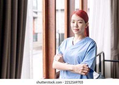 Portrait Of Asian Therapist Woman Nurse Wearing Medical Scrubs In The House Of Patient. Caregiver Visit At Home. Home Health Care And Nursing Home Concept.