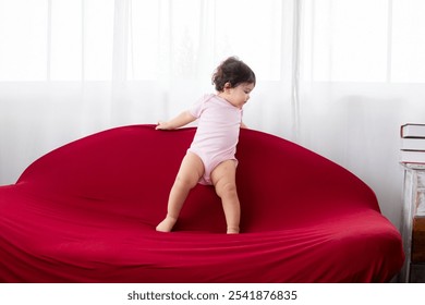 Portrait Asian toddler girl infant climbing red sofa at home looking to window, happy healthy cute baby kid soft skin waiting for mother or playing alone, Children's learning and child development. - Powered by Shutterstock