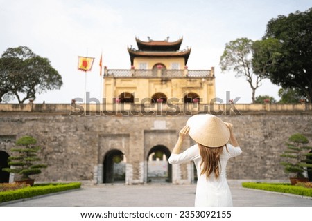 Portrait of Asian Vietnamese woman with Vietnam dress and straw hat travel at Imperial Citadel of Thang Long, Tourist attraction landmark in urban city town of Hanoi, Vietnam. People lifestyle.