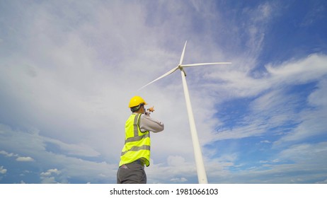 Portrait Of Asian Windmill Engineer Man, Worker Working On Site At Wind Turbines Field Or Farm, Renewable Clean Energy Source. Eco Technology For Electric Power. Industry Nature Environment. People