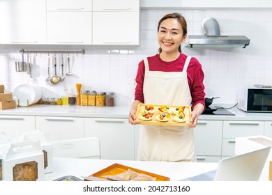 Portrait Of Asian Woman Bakery Shop Owner Using Laptop Computer Advertising Online Bakery Store On Social Media In The Kitchen. Small Business Entrepreneur And Online Marketing Food Delivery Concept