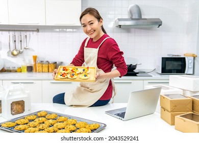 Portrait Of Asian Woman Bakery Shop Owner Using Laptop Computer Advertising Online Bakery Store On Social Media In The Kitchen. Small Business Entrepreneur And Online Marketing Food Delivery Concept
