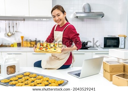 Portrait of Asian woman bakery shop owner using laptop computer advertising online bakery store on social media in the kitchen. Small business entrepreneur and online marketing food delivery concept