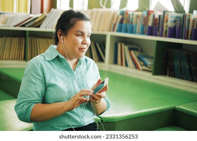 Portrait of Asian woman with blindness disability wearing earphones using smart phone with voice accessibility for persons with visual impairment disabilities in creative workplace library. - Shutterstock ID 2331356253